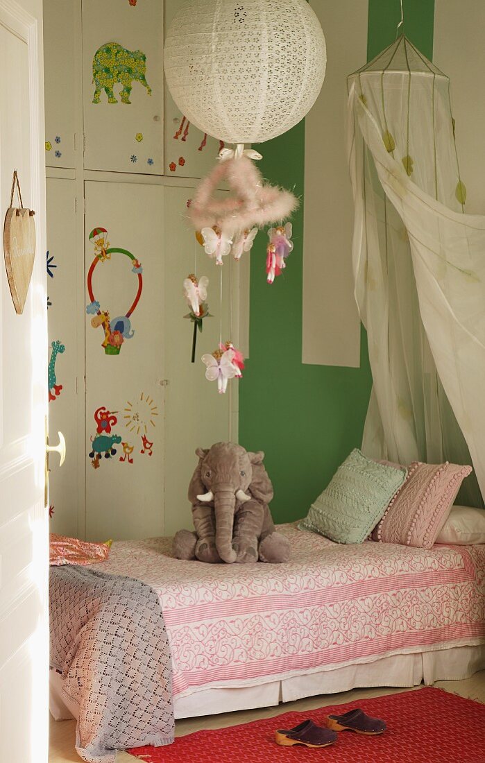 Bett mit Stofftier in einem Kinderschlafzimmer mit Einbauschrank und grüner Wand