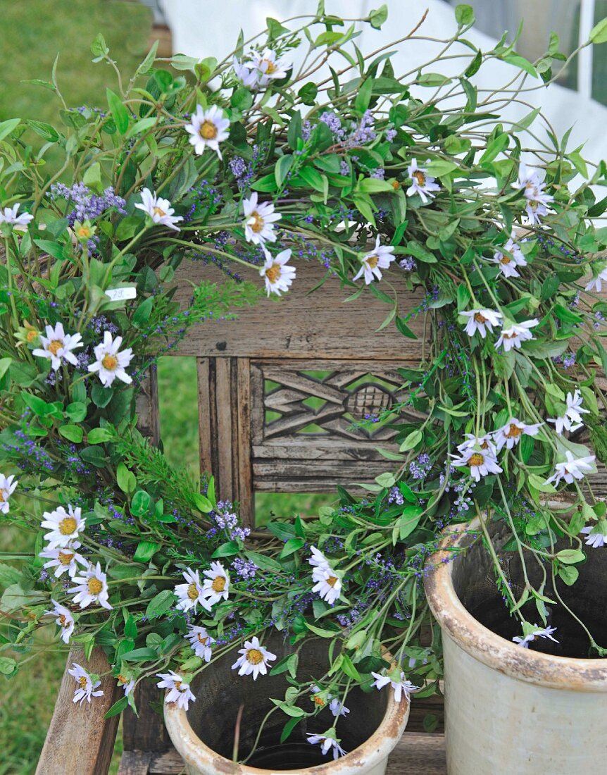 Wreath of flowers with ox-eye daisies and terracotta pots on wooden chair