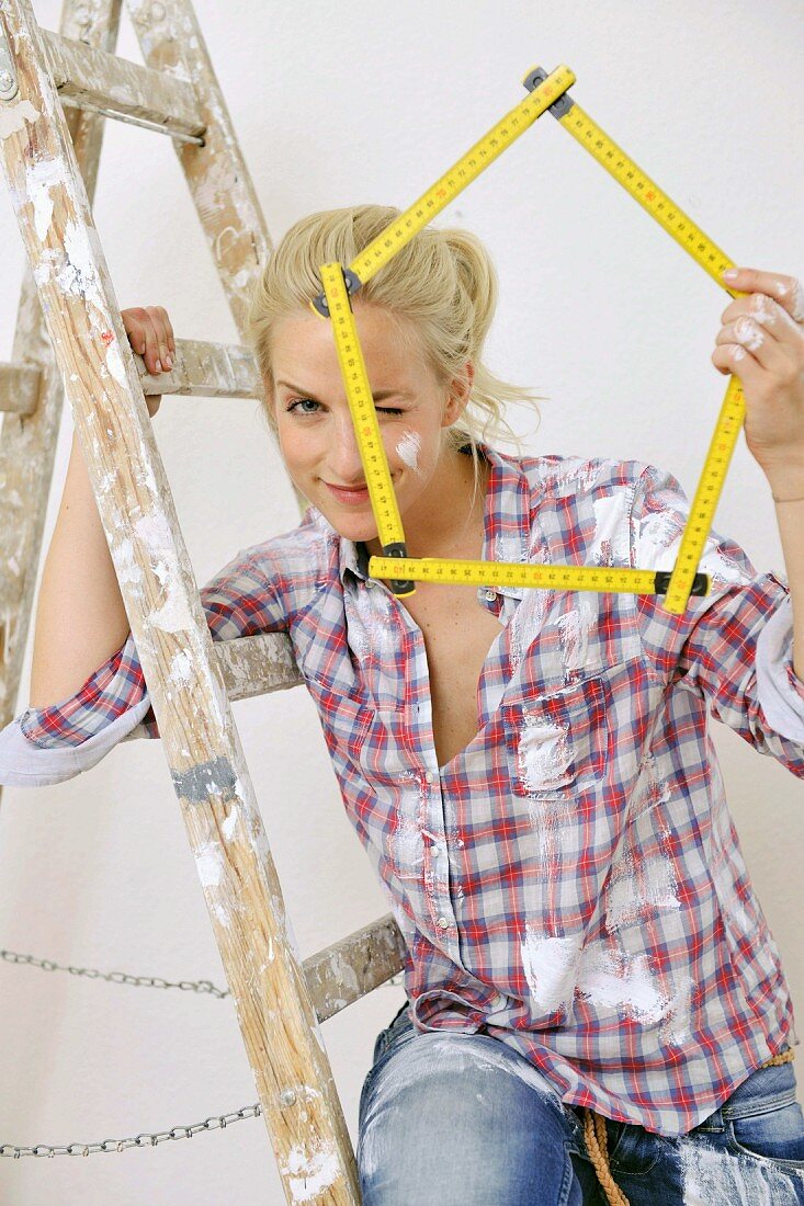 Renovierungsarbeiten - Frau sitzt auf der Leiter und hält einen Meterstab in der Hand