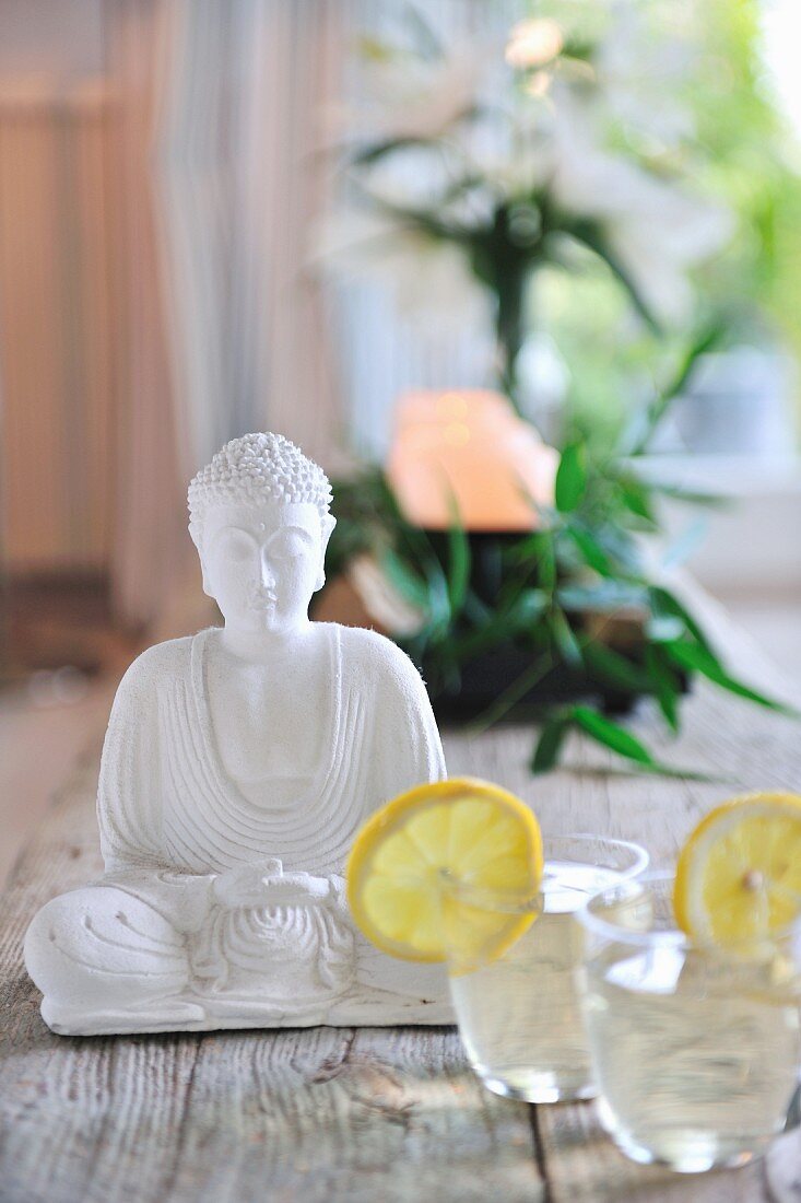 Erfrischungsgetränke neben sitzender Buddhafigur aus weißem Stein auf Holzdielen