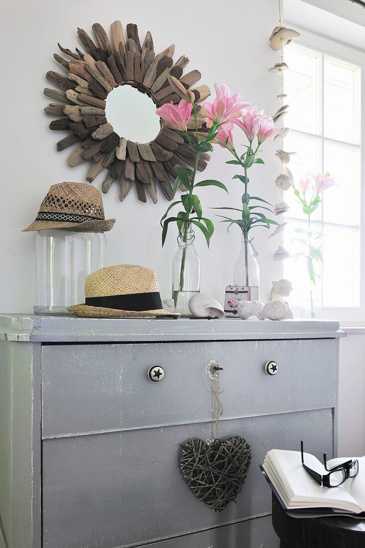 Vases of flowers on white-painted chest of drawers and mirror with sun-shaped frame on wall
