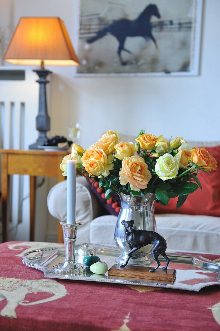 Tablett mit Rosenstrauss in Silbervase und brennender Kerze auf Couchtisch in traditionellem Wohnzimmer