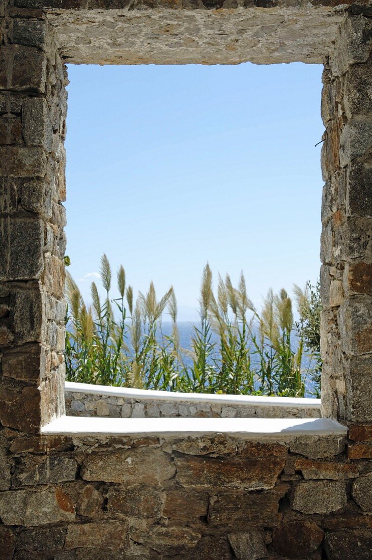 Blick durch Fensteröffnung in Natursteinmauer auf das Meer