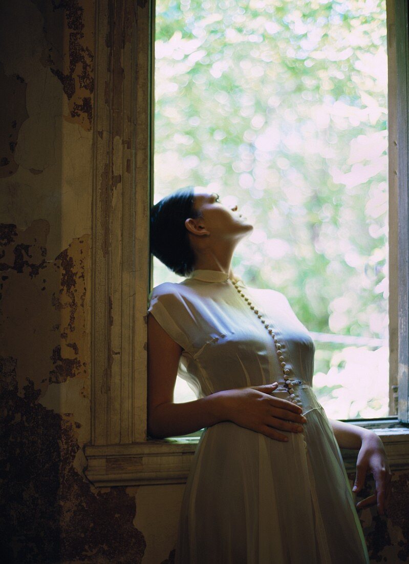 Elegant gekleidete junge Frau lehnt sich aus dem Fenster