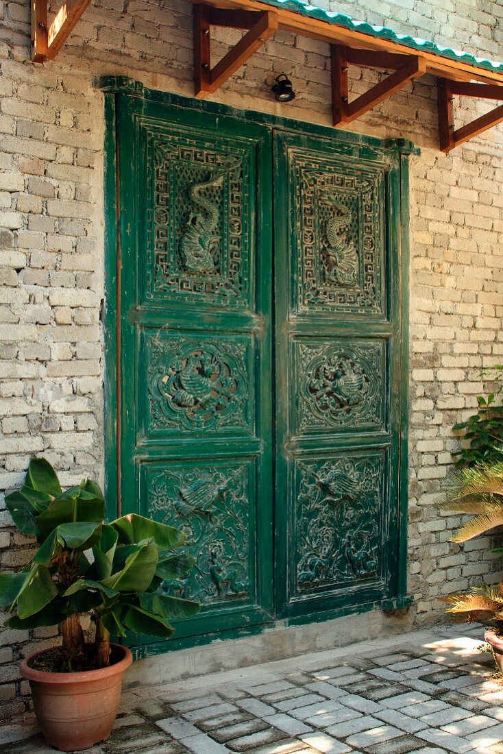 Green-painted, carved front door and small porch on brick facade