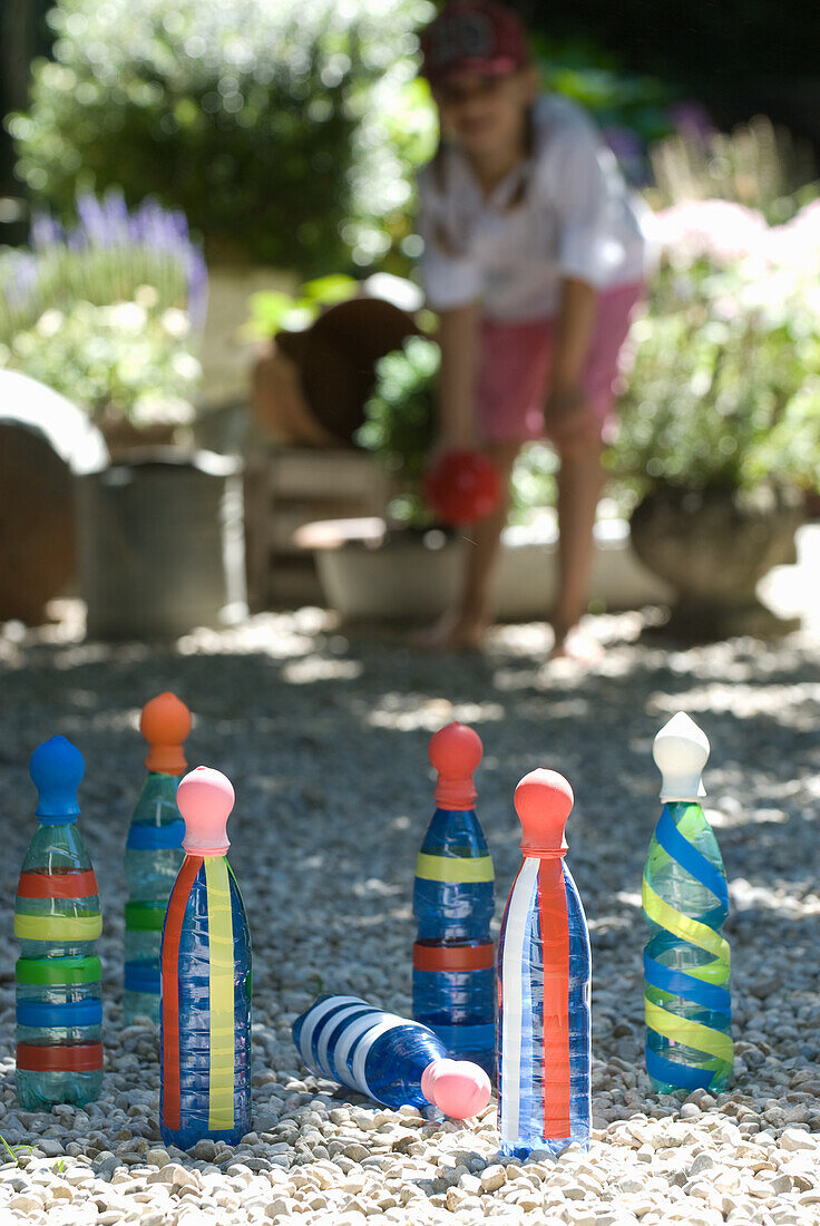 Child playing skittles with colourful bottles in the gravel garden