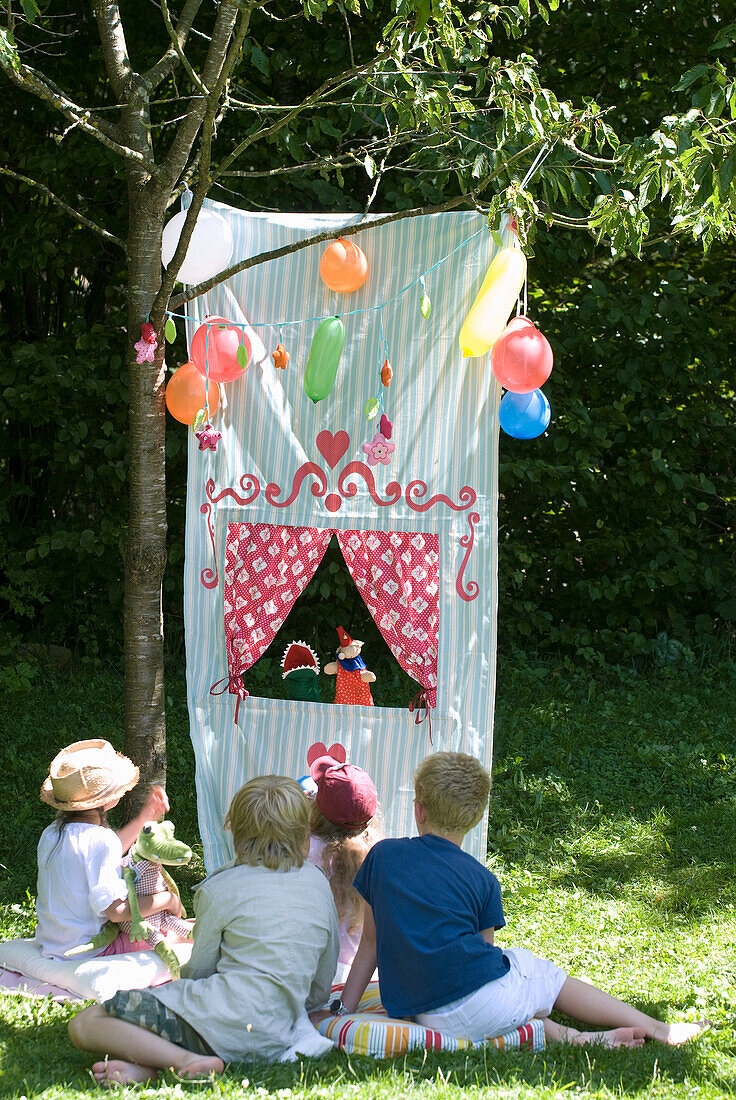 DIY box theatre made of fabric with children and balloons in a sunny garden