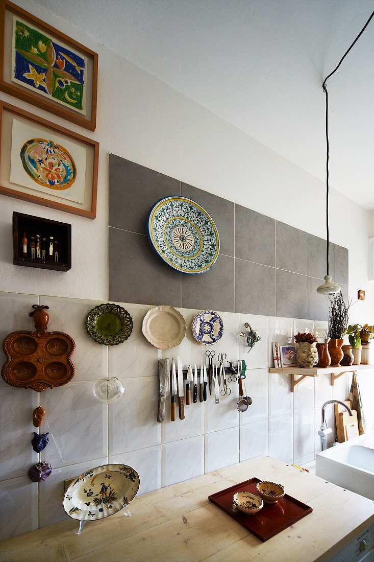 Messer und Scheren an Magnetbord, umgeben von bunten Sammeltellern am Wandfliesenmix einer improvisierten Küchenzeile