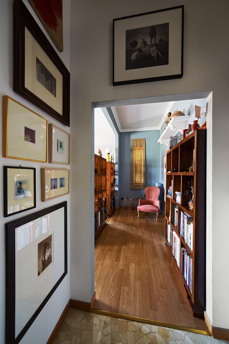 Blick von Vorraum mit Bildergalerie entlang eines Bücherregals über die Parkettflucht des Wohnzimmers auf rosefarbenen Barockstuhl