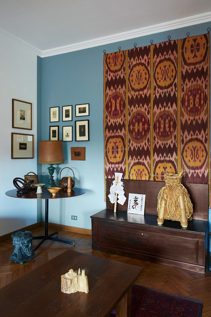 Antique collectors' items and large, decorative kilim on pale blue living room wall