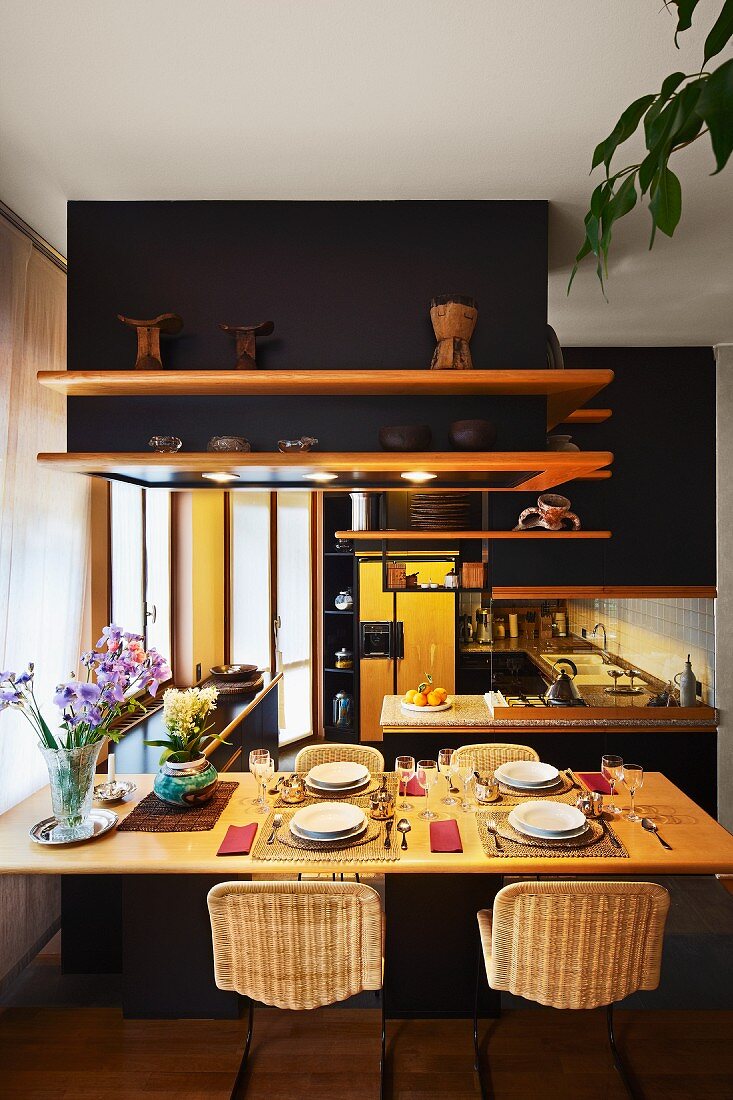 Gedeckter Esstisch in offener Küche mit Regalen an abgehängten, schwarz getönten Decken-Einbauten
