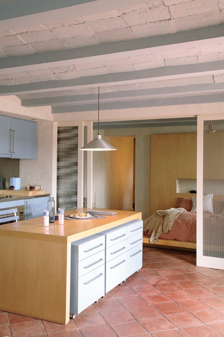 Moderne, offene Küche mit mediterraner Rippendecke und Terracottaboden; durch transluzente Schiebetüren abgetrennter Schlafbereich im Hintergrund