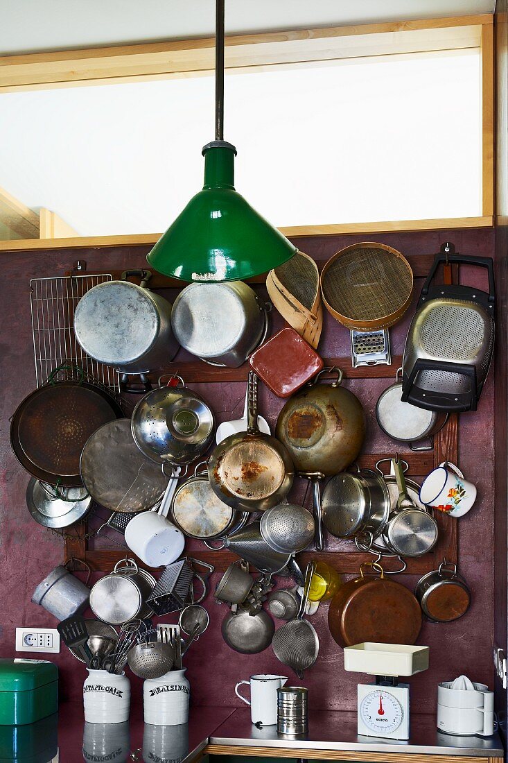 Pots and pans hanging on wall rack below transom window and vintage pendant lamp with green metal lampshade