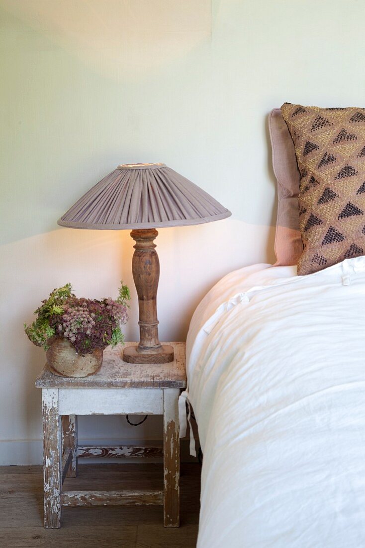 Simple bedroom with table lamp on rustic stool next to bed