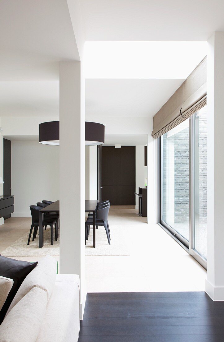 View into open-plan interior with black dining set below designer pendant lamp next to floor-to-ceiling terrace windows