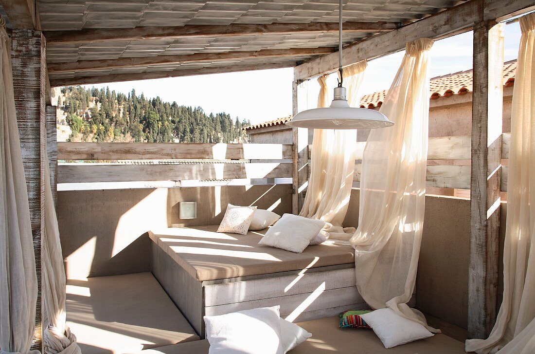 Sommerstimmung auf Veranda mit gemütlichem Bettlager und luftigen Vorhängen am Vordach aufgehängt