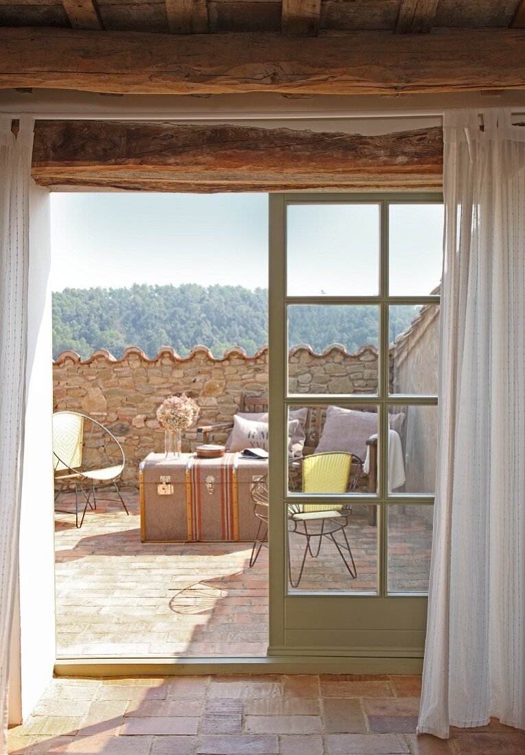 View through French windows onto Mediterranean roof terrace with wire furniture and travelling trunk used as table