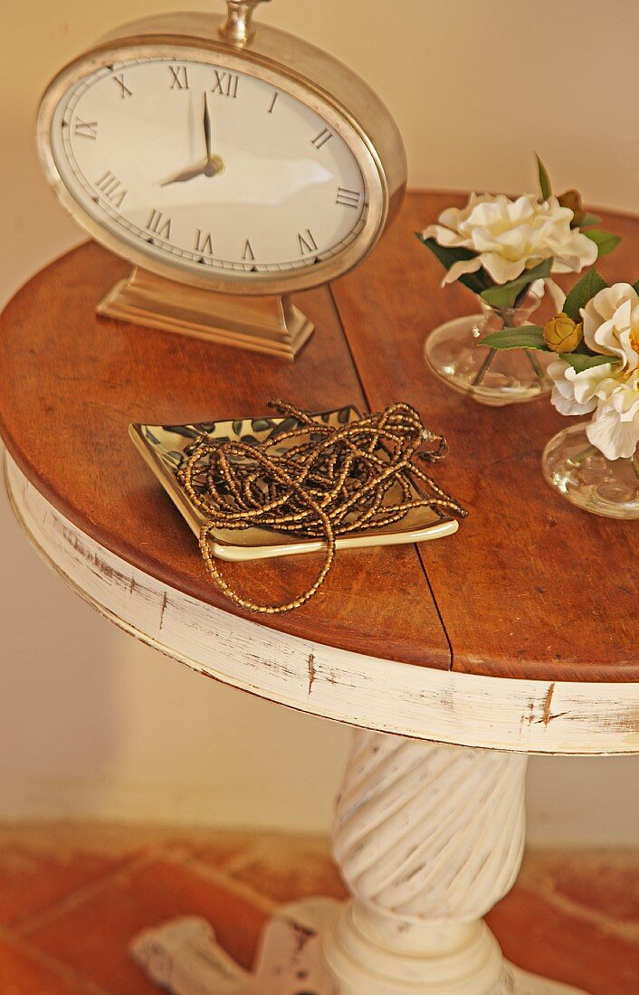 Altmodische Tischuhr und Perlenkette in Schale auf einem Beistelltisch im mediterranen Vintagelook