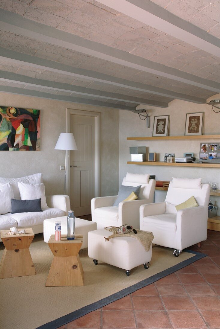 Helle Polstermöbel auf Rollen und Holzhocker als Beistelltische in mediterranem Wohnzimmer mit Rippendecke und Terracottafliesen
