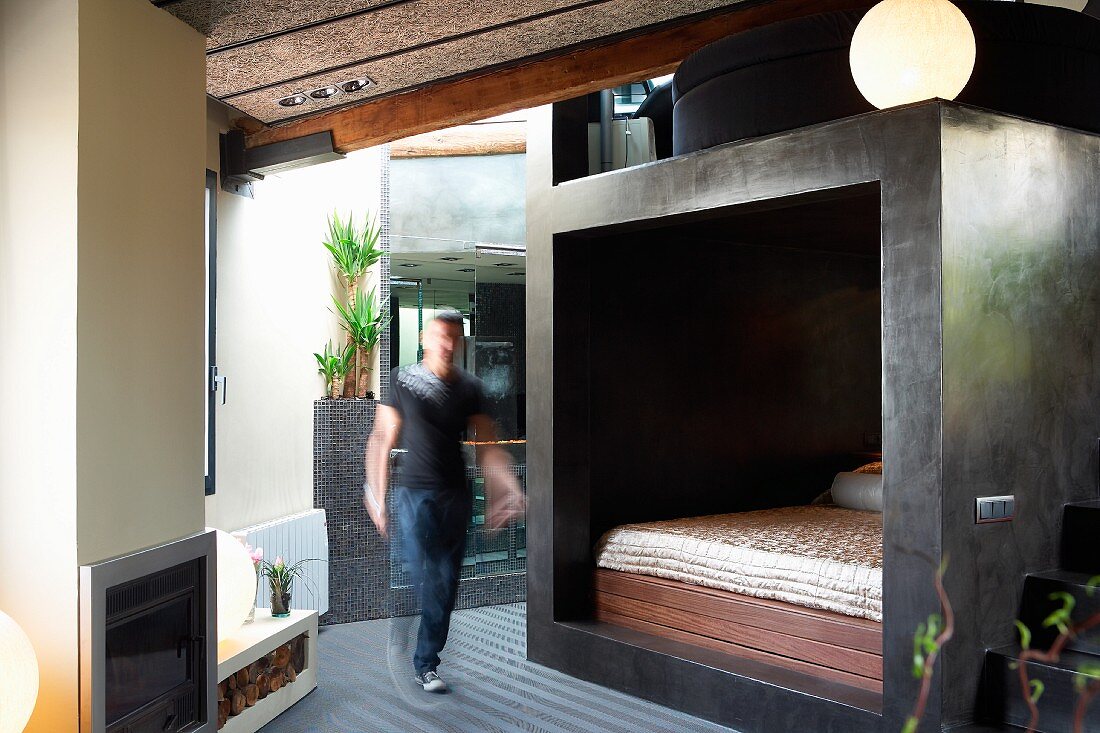 Mann vor Schlafbereich mit grau verspachtelten Wänden in offenem, modernem Wohnraum