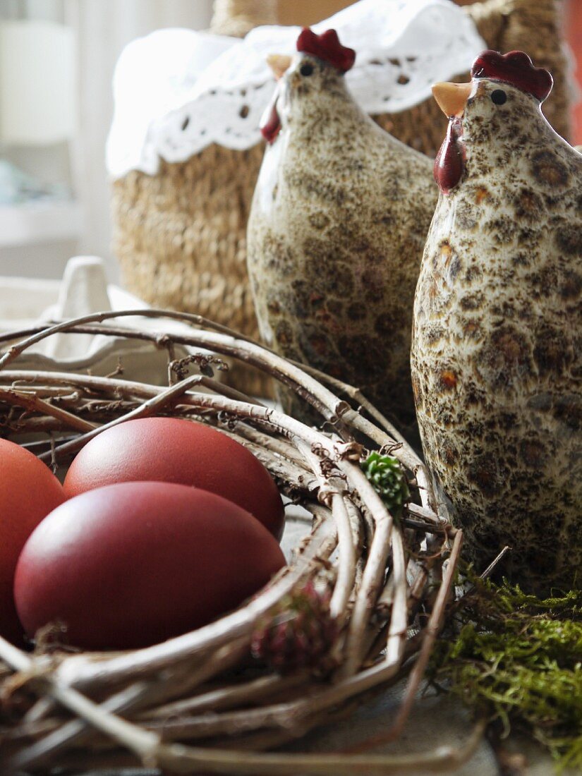 Hühnerfiguren aus Porzellan und Nest mit farbigen Eiern
