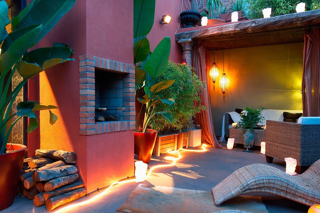 Twilight atmosphere on Mediterranean terrace with lit lanterns and light rope next to house with red lime washed facade