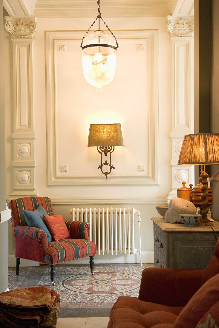 Hallway with stylish antique lamps and delicate armchair on mosaic floor