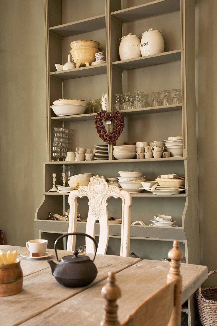 Open-fronted shelving in same colour as walls, rustic wooden table and antique chairs create cosy vintage look in kitchen-dining room