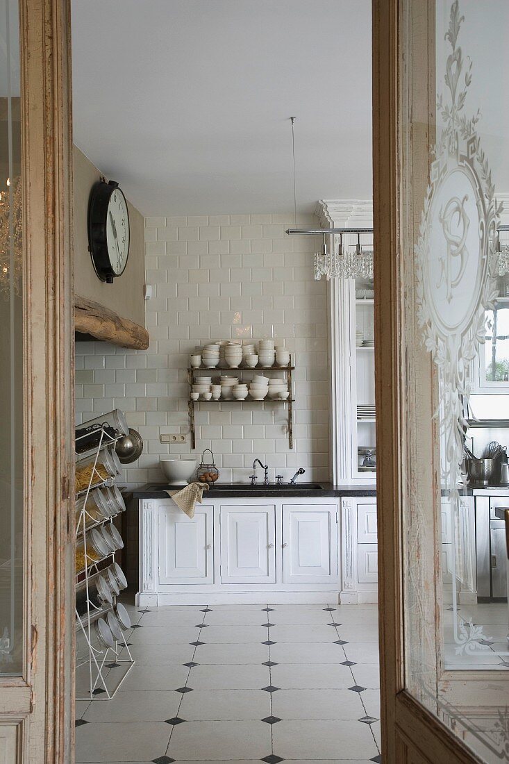 Blick durch offene Tür in schlichte Landhausküche mit weißem Fliesenboden und dunklen Einlegerfliesen
