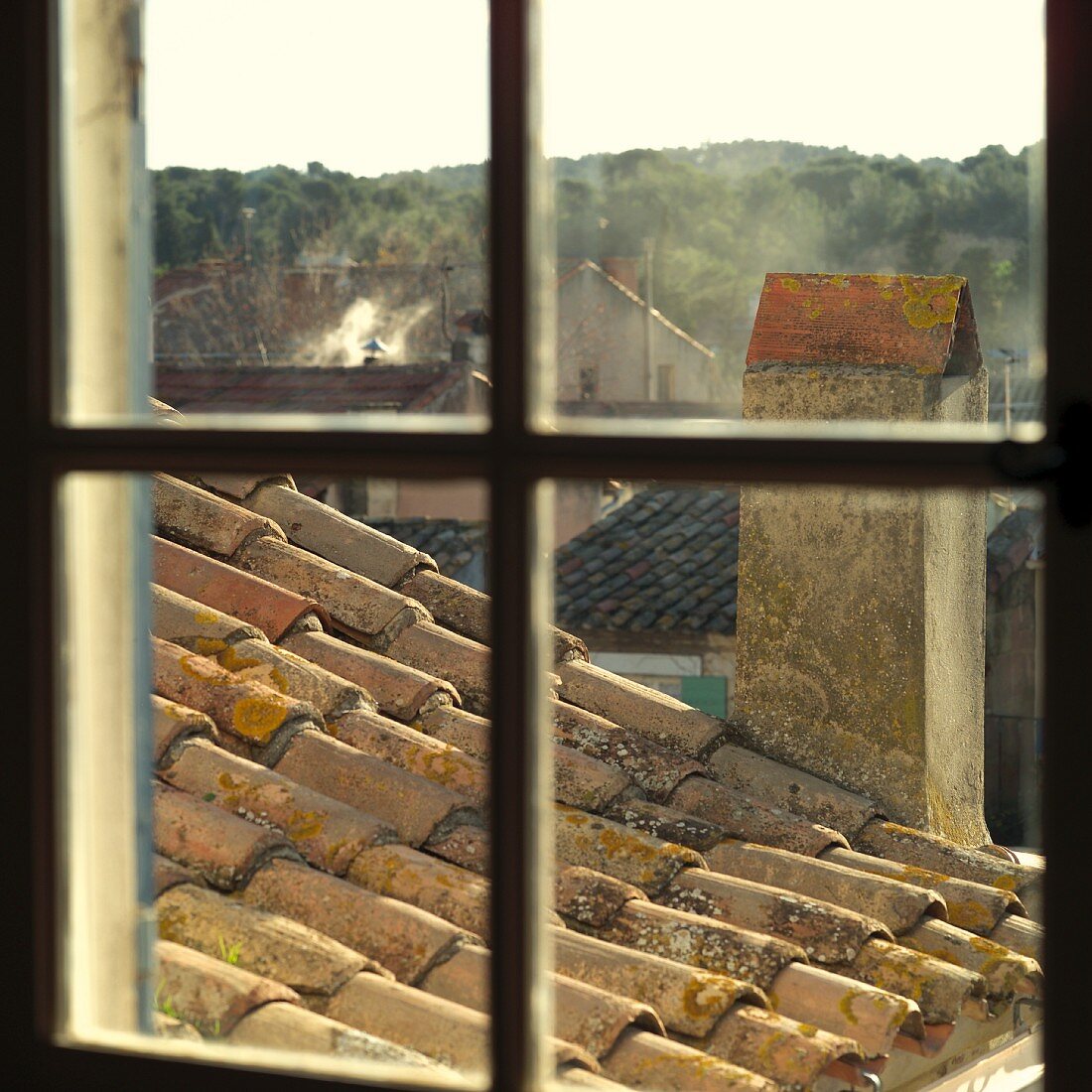 Blick durch ein Fensterkreuz auf Kamin und mediterranes Dach mit Mönch- und Nonnendeckung