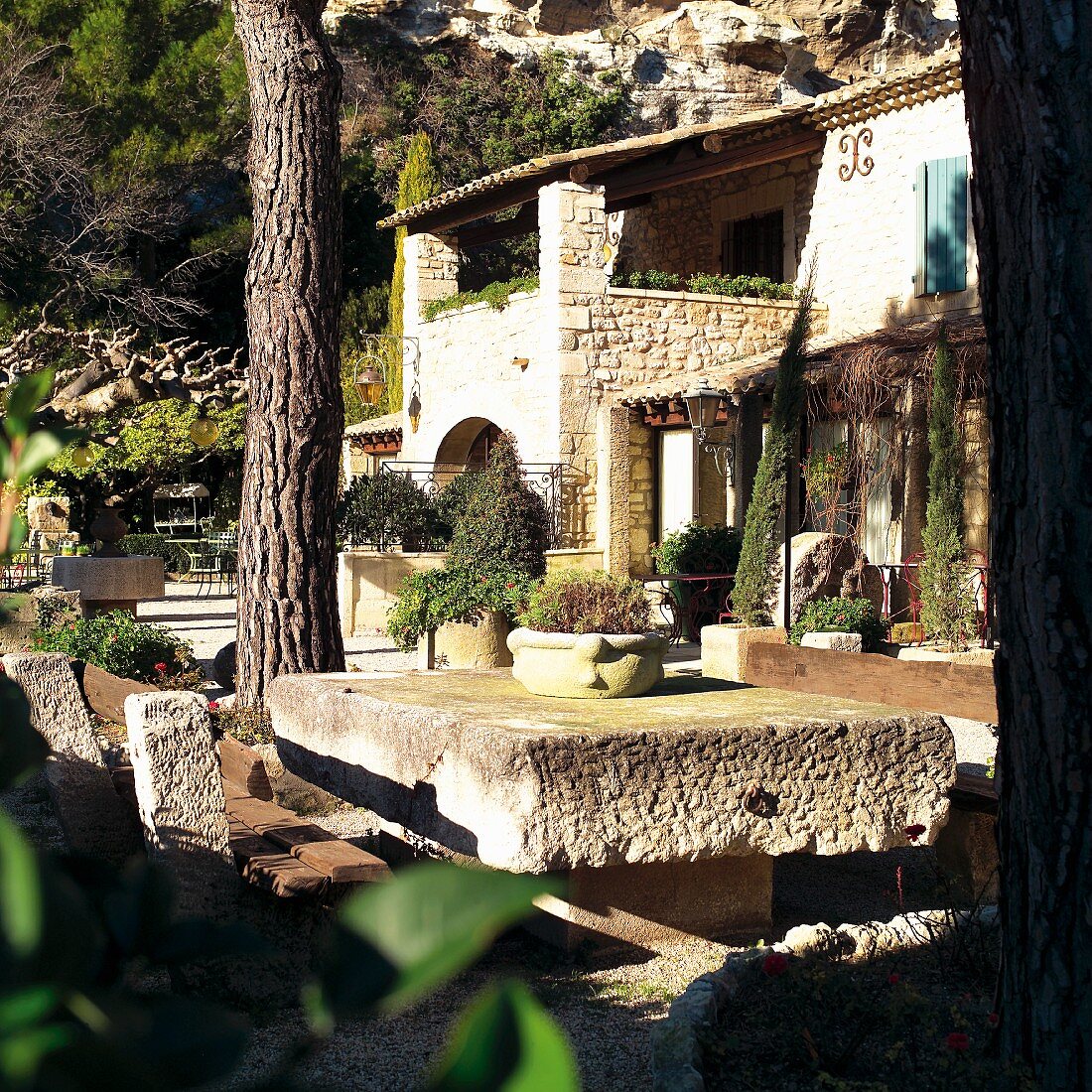 Mediterrane Hausanlage und Terrassenplatz mit verwitterter Stein Tischplatte vor Berg Felswand
