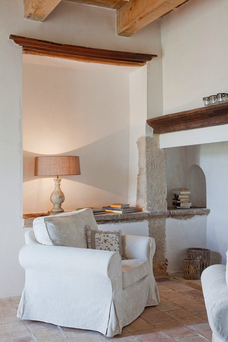 White armchair in corner of living room in front of illuminated niche in Mediterranean country house