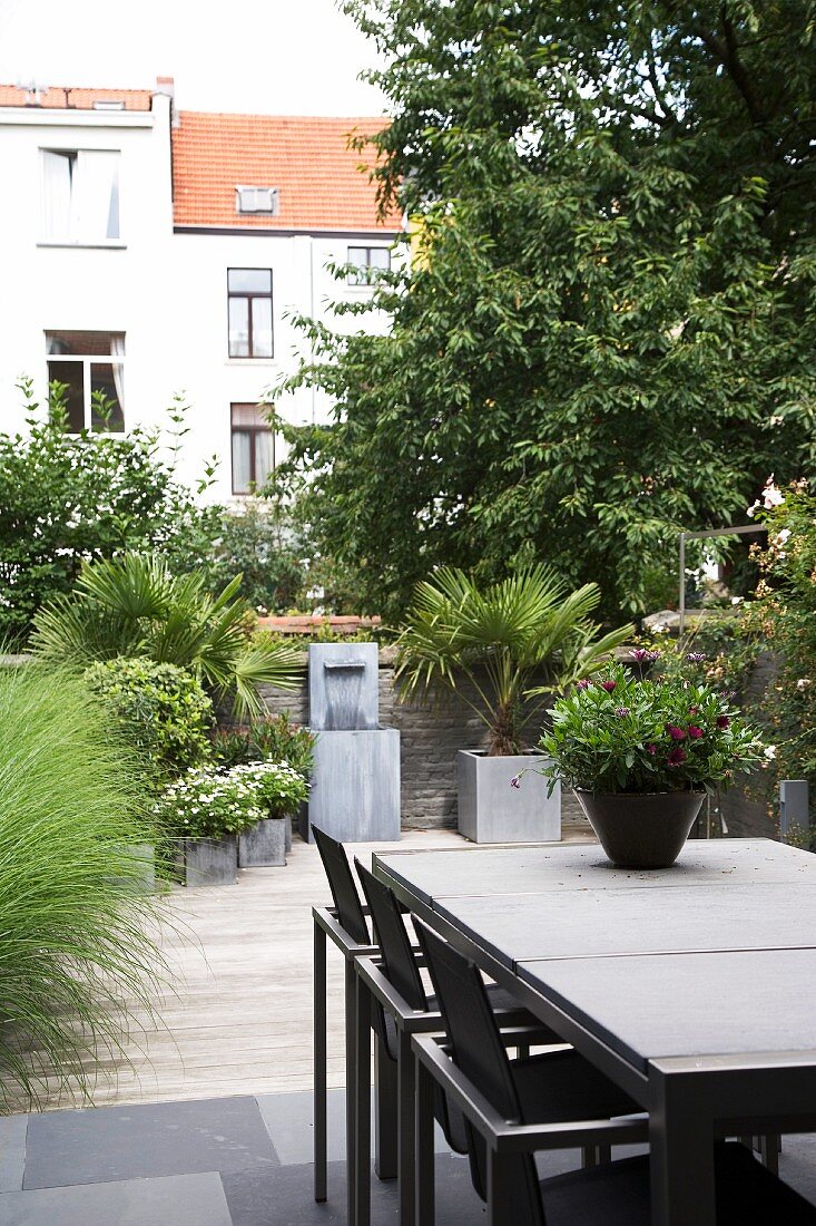 Designer-Outdoortisch und Stühle auf Terrasse mit Pflanzentöpfen im Innenhof einer Wohnanlage