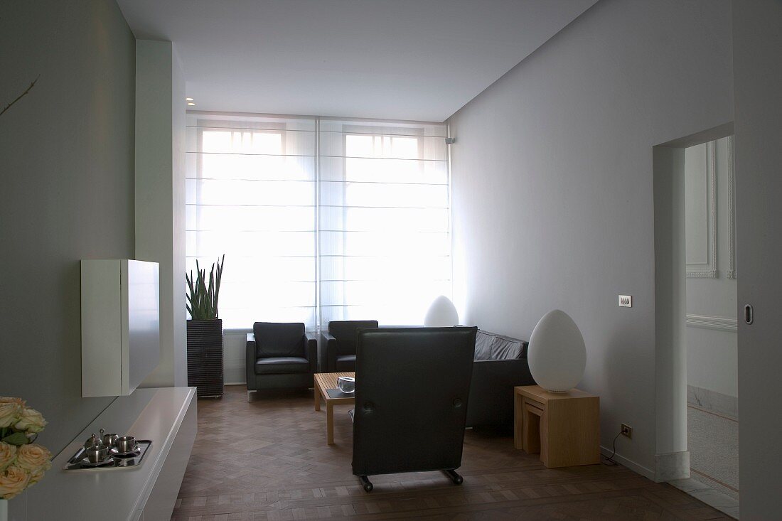 Minimalistischer Wohnraum mit schwarzer Ledergarnitur in Loungeecke vor Fenster