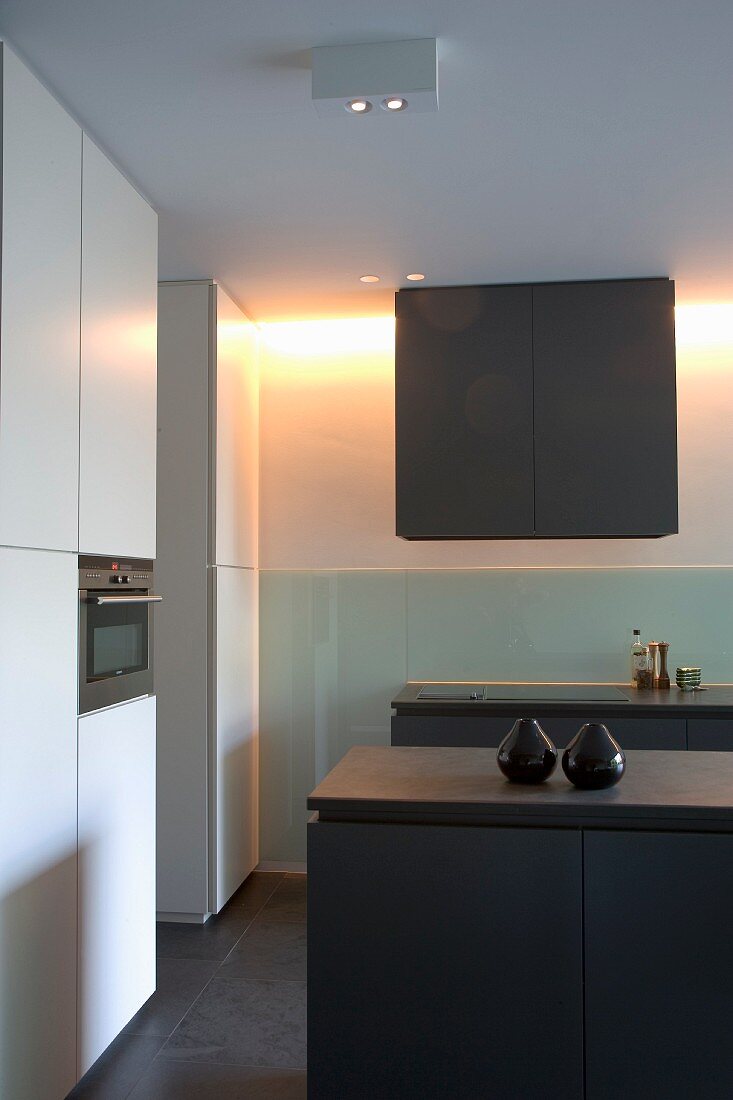 Dunkelgrauer Hängeschrank an Wand unter indirekter Beleuchtung in Designer-Küche