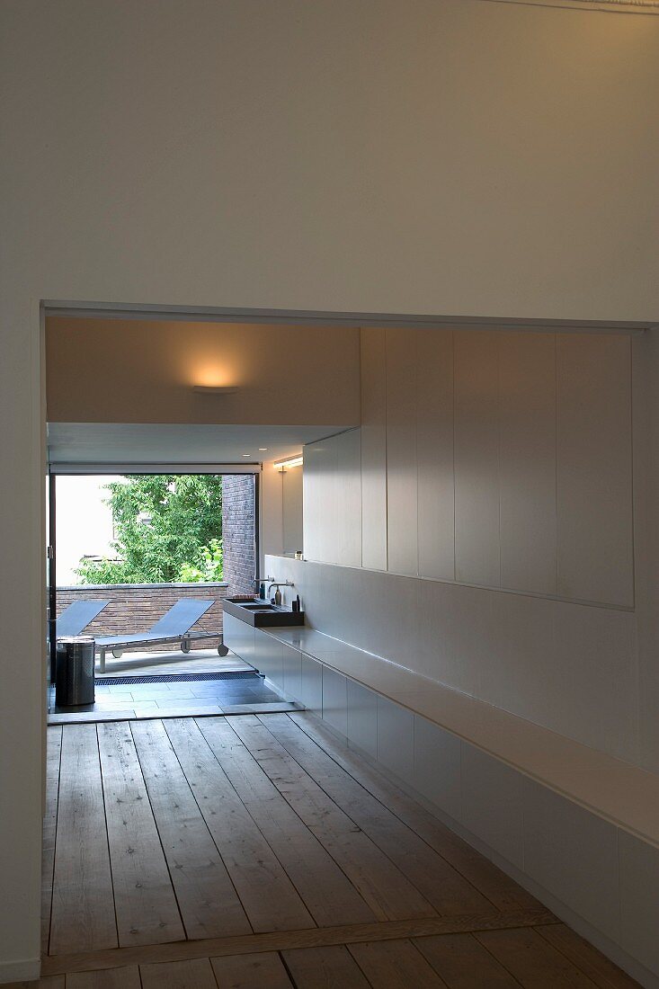 Designer bathroom with wooden board floor and open terrace door with view of loungers