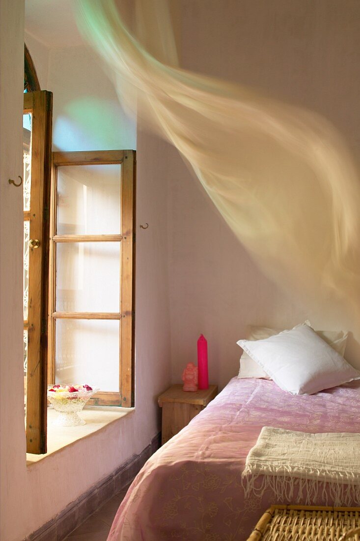 Schlichtes Schlafzimmer - Rosa Tagesdecke auf Bett vor offenem Fenster mit wehendem Vorhang