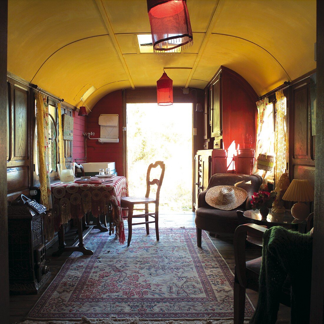 Gemütlicher Wohnraum in umgenutztem Zugwaggon mit Orientteppich und roten Lampions an der gelben Decke