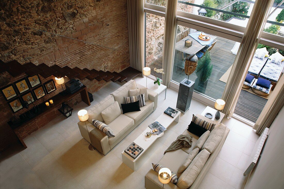 Blick von oben auf Sofagarnitur in einem grossen Wohnzimmer mit Fensterfront und Natursteinwand