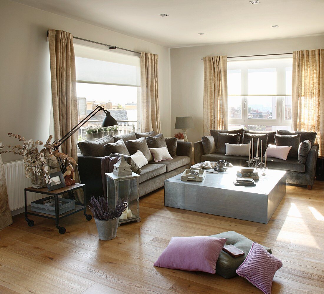 Wohnzimmerecke mit modernem Bodentisch aus Edelstahl und grau braune Polstercouch vor Fenster