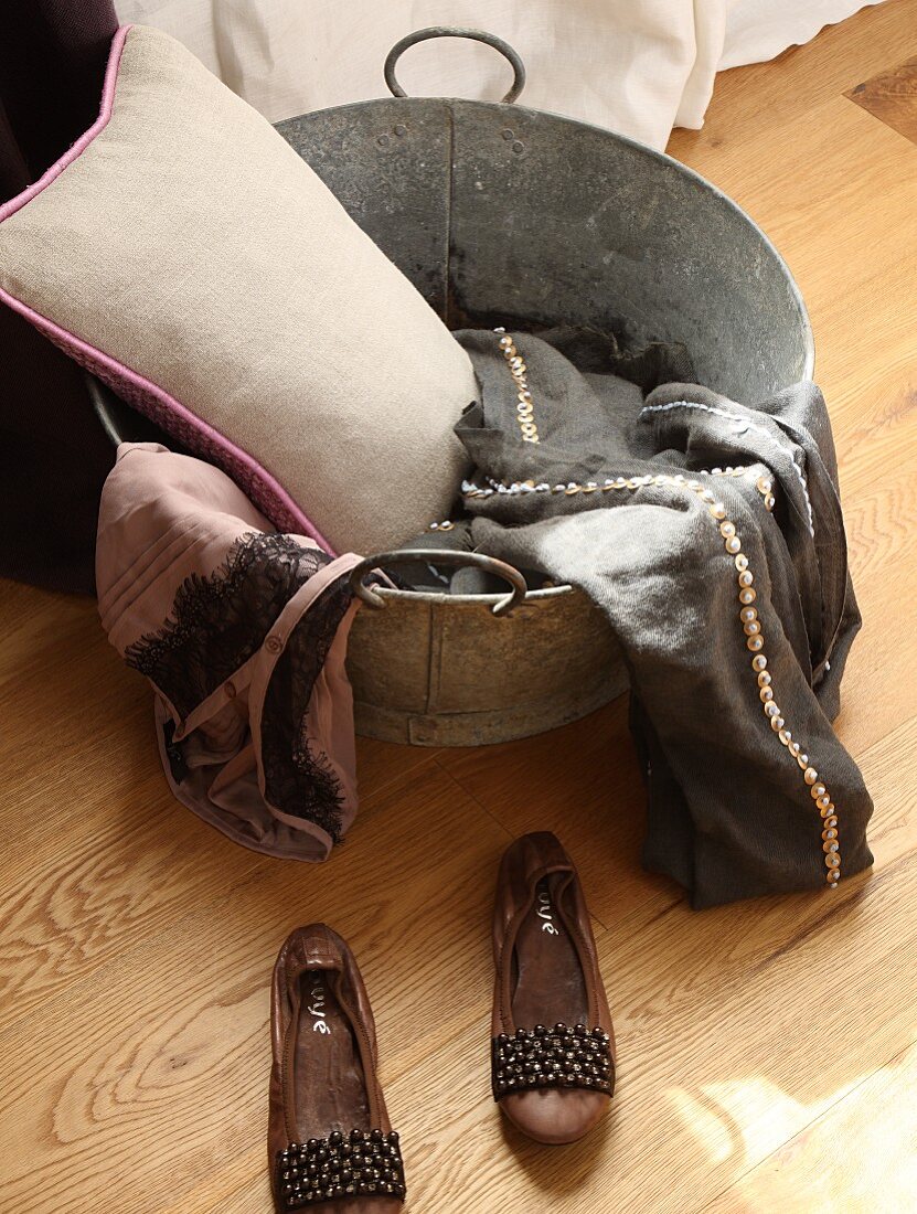 Ladies' shoes next to cushion and clothes in zinc tub on wooden floor