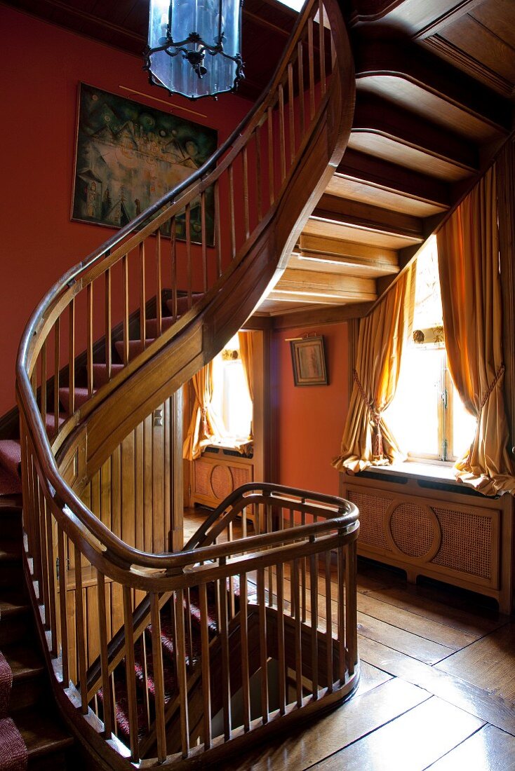 Traditional stairwell with winding wooden staircase against rust brown walls and old board floor