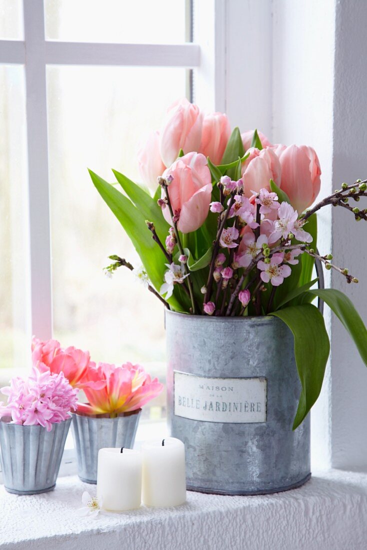 Tulpen und blühende Pfirsichzweige im größeren Gefäß, Tulpen und rosa Hyazinthen in kleinen Zinkgefäßen am Fenster