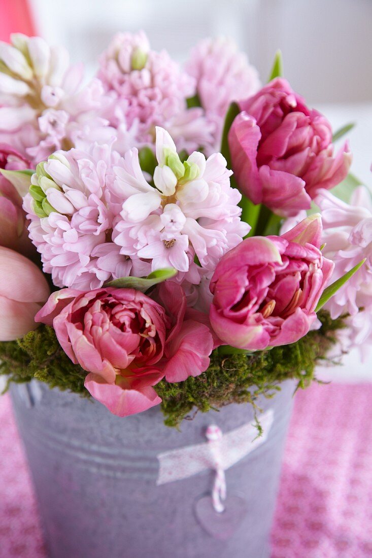 Mooskranz mit Strauss aus rosa Hyazinthen und Tulpen in einem Zinkgefäß
