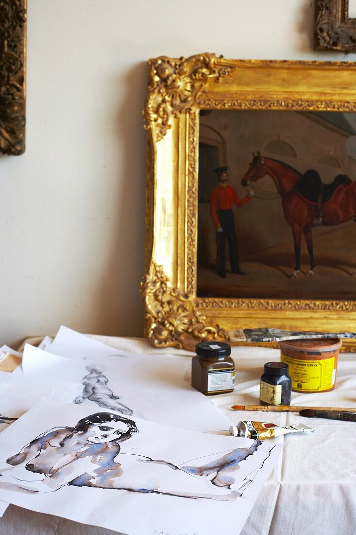 Artist's studio: original paintings, painters' utensils and gilt-framed oil painting on table