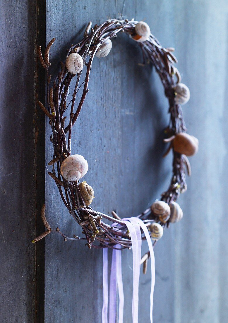 Wreath decorated with snail shells hanging on wooden wall