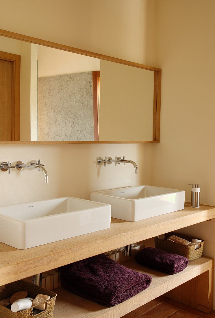 Washstand with twin basins and shelf in base unit in corner of simple bathroom