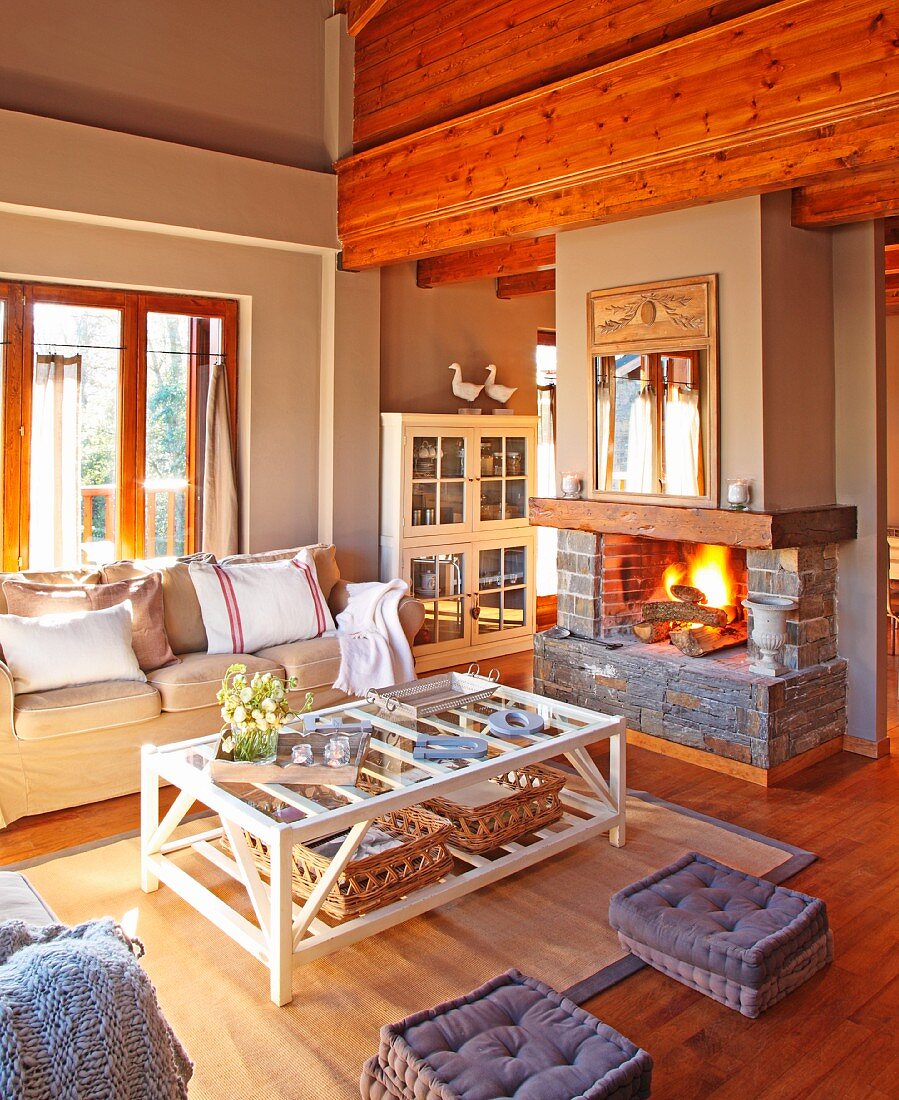 Living area with coffee table made of pale wooden slats and comfortable sofa in front of country-style open fire