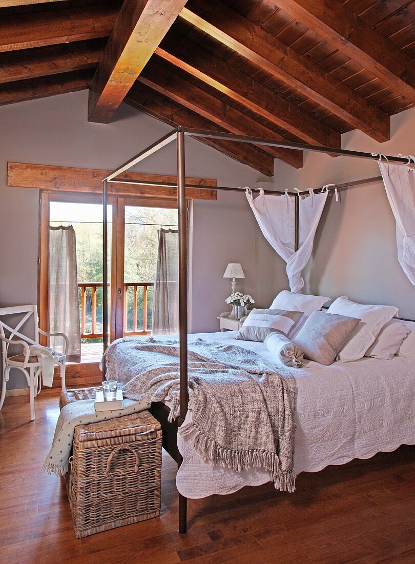Himmelbett mit Metallgestell und weisser Bettwäsche im Dachzimmer mit rustikaler Holzbalkendecke