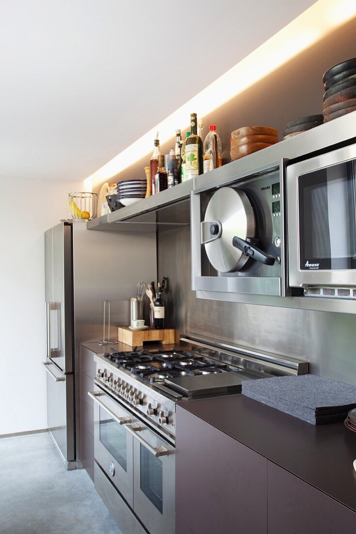 Stainless steel and uniform dark surfaces in designer kitchen with fitted professional appliances